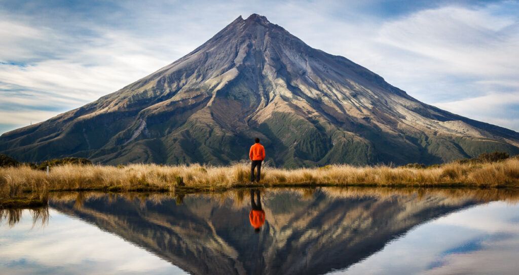 Man standing in front of lake looking at Mt Tarakani in Egmont National Park